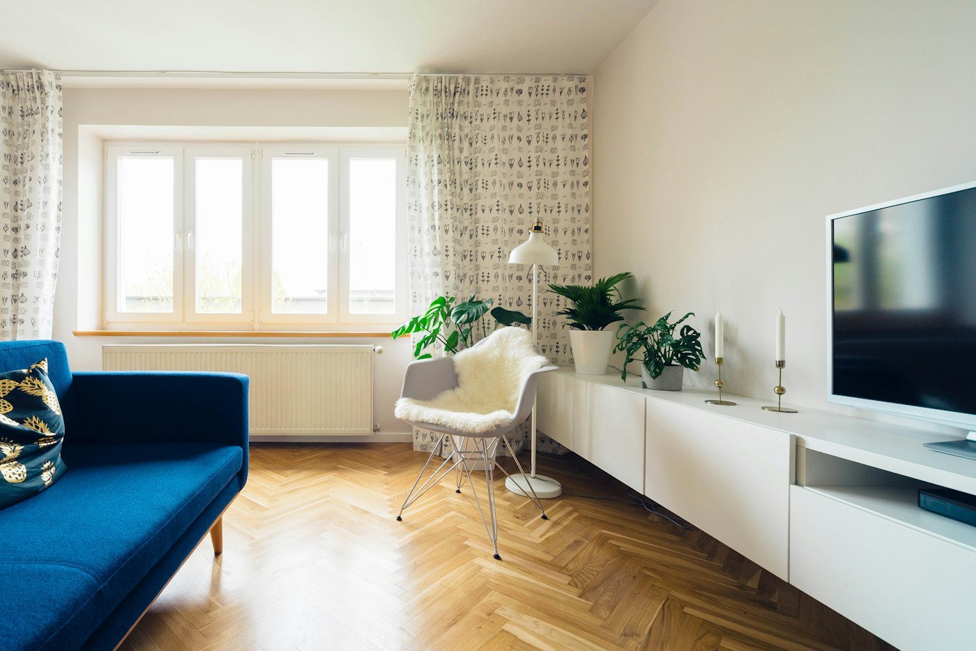 A living room with a blue sofa, herringbone wood floor, and a long white sideboard